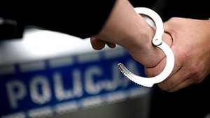zdjęcie kolorowe: na tle policyjnego radiowozu kajdanki zakładane na ręce zatrzymanego