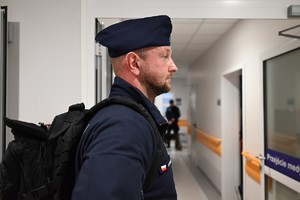 Zdjęcie przedstawia policjanta z założonym czarnym plecakiem na plecach