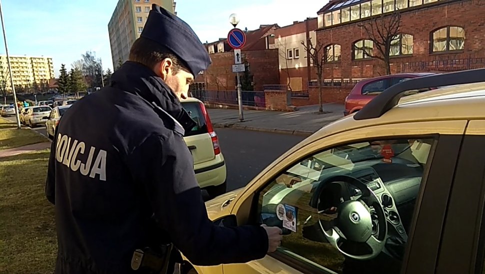 Na zdjęciu widać policjanta obok samochodu w tel widać budynki 