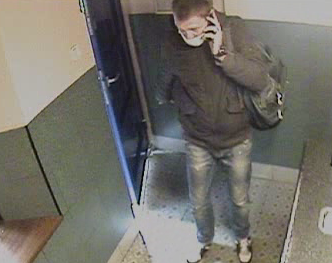 zdjęcie kolorowe zapisu monitoringu, gdzie widoczny jest mężczyzna wchodzący do lombardu, ubrany w ciemna kurtkę i niebieskie spodnie z założoną maseczką ochronną na twarzy i trzymający w lewej ręce przy uchu telefon komórkowy