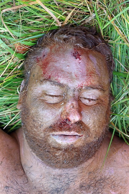 zdjęcie kolorowe:zdjęcie przedstawia tors i głowę zmarłego rudego mężczyzny z brodą, który leży na trawie na trawie