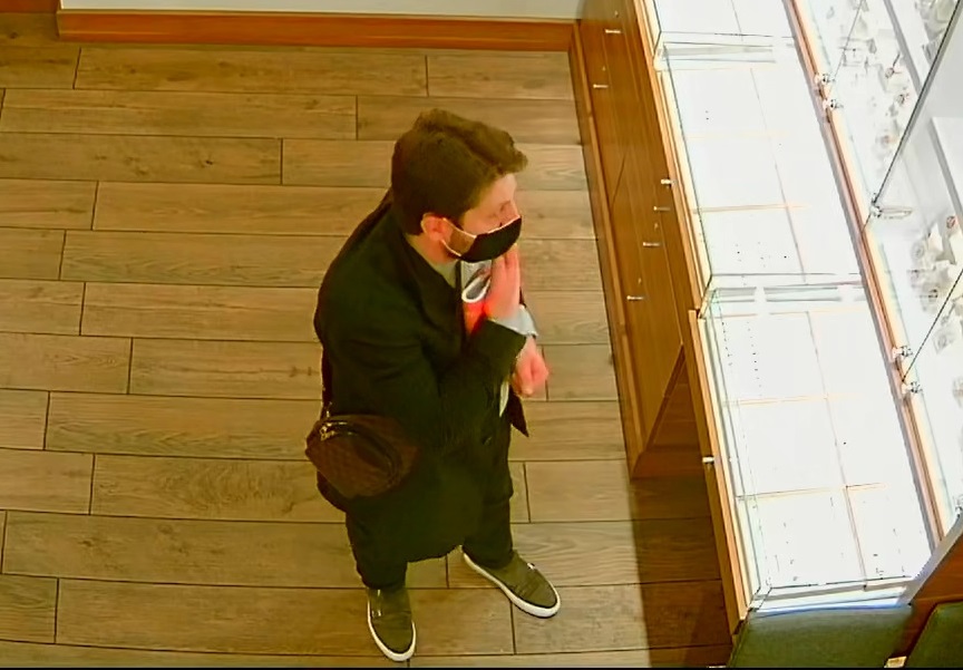 zdjęcie kolorowe: screen z monitoringu sklepowego przedstawiający mężczyznę ubranego w ciemne spodnie, ciemny płaszcz, szary sweter z założona czarna maseczka ochronna na twarzy i rozmawiający przez telefon komórkowy, prawy profil