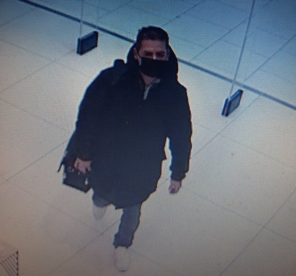 zdjęcie kolorowe: zrzut obrazu z monitoringu sklepowego przedstawiający mężczyznę w czarnej długiej kurtce, ciemnych spodniach i białych butach sportowych, gdzie na twarzy ma założoną czarna maseczkę ochronną