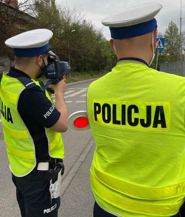 zdjęcie kolorowe: dwóch policjantów katowickiej drogówki podczas kontroli prędkości pojazdu w rejonie oznakowanego przejścia dla pieszych