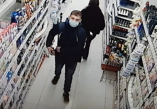 zdjęcie kolorowe: mężczyzna w czarnych spodniach i w czarnej kurtce z niebieska maseczka ochronna na twarzy w alejce sklepu kosmetycznego