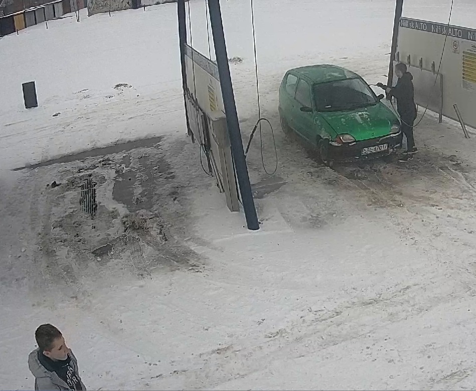 zdjęcie kolorowe: myjnia samochodowa, zielony samochód osobowy i dwóch mężczyzn podejrzewanych o jej zniszczenie