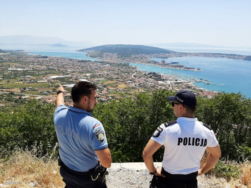 zdjęcie kolorowe:polski policjant wspólnie z chorwackim policjantem na wzgórzu z widokiem na nadmorskie miasteczko
