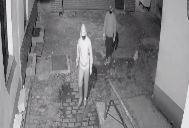 zdjęcie czarno-białe: dwóch zamaskowanych mężczyzn idących przez podwórko, tuz przy kamienicy