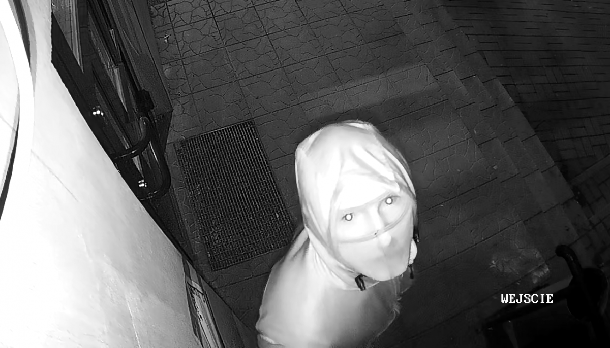 zdjęcie czarno-białe: ujęcie z kamery monitoringu zamaskowany mężczyzna patrzący na kamerę monitoringu