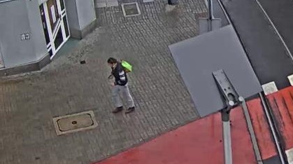 zdjęcie z monitoringu miejskiego: mężczyzna w centrum Katowic ubrany w szare spodnie, ciemny sweter, niosący na prawym ramieniu zielona torbę