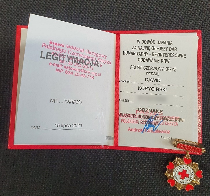 zdjęcie kolorowe: otwarta legitymacja odznaczenia „Zasłużony Honorowy Dawca Krwi I Stopnia” wydana przez Śląski Oddział Okręgowy Polskiego Czerwonego Krzyża w Katowicach, z dnia 15 lipca 2021 roku , nr 350/9/2021 dla Pana Dawida Korycińskiego