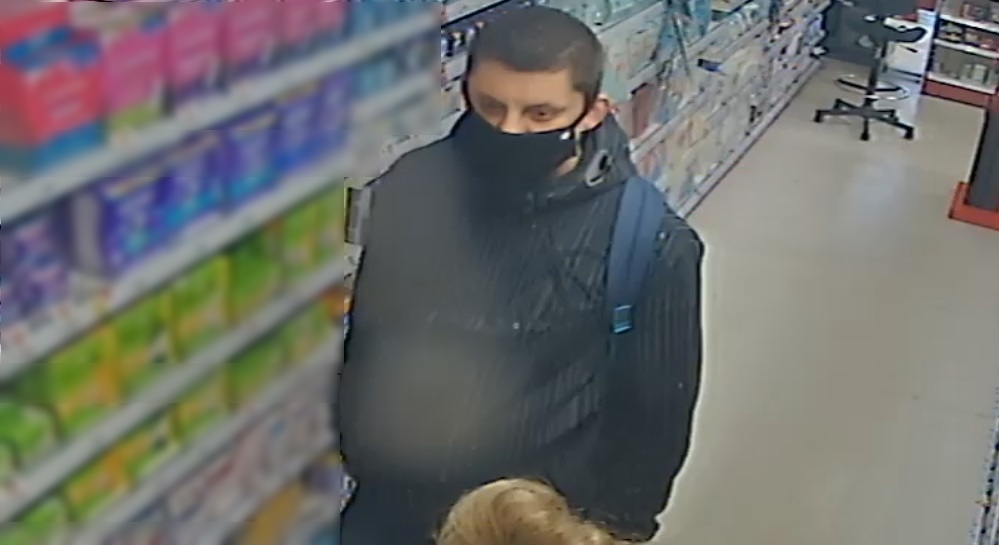 zdjęcie kolorowe: mężczyzna podejrzewany o kradzież perfum ubrany w czarną kurtkę i czarna maseczkę ochronną zakrywającą twarz