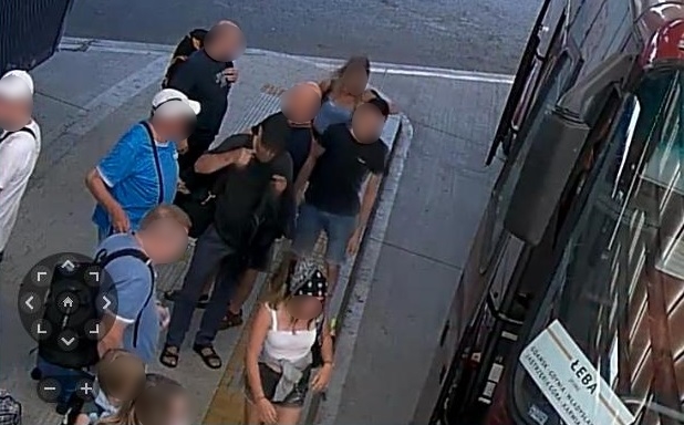 zdjęcie kolorowe: dworzec autobusowy, grupa ludzi oczekująca na peronie przed autobusem i podejrzewany o kradzież kieszonkową mężczyzna ubrany był w ciemnoszarą koszulkę z krótkim rękawem, ciemne spodnie, sandały i czapkę z daszkiem koloru czarnego, który zaklada czarna maseczkę ochronna na twarz