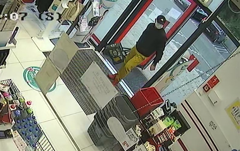 zdjęcie kolorowe: wysoki mężczyzna ubrany w musztardowe spodnie, ciemną kurtkę, czarna czapkę z daszkiem z założoną maseczka ochronna na twarzy wchodzący do sklepu