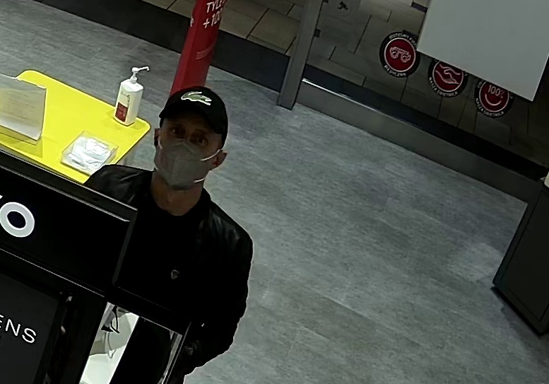 zdjęcie kolorowe: mężczyzna w czarnej czapce z daszkiem i czarnej kurtce z maseczka ochronna założoną na twarz spoglądający w kamerę monitoringu
