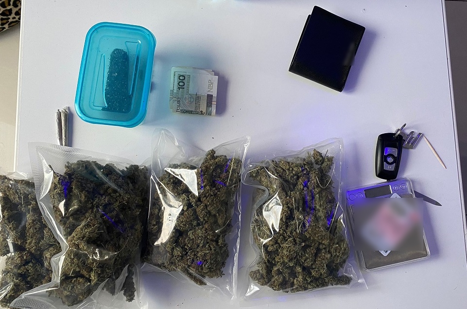 zdjęcie kolorowe: na blacie stołu zabezpieczone 4 worki z marihuaną, gotówka, skręty, waga, portfel i kluczyk z samochodu