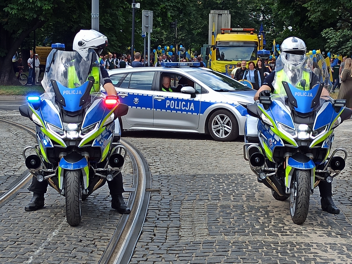 zdjęcie kolorowe: dwóch policjantów katowickiej drogówki na motorach służbowych i policyjny radiowóz oczekujący na rozpoczęcie przemarszu uczestników zgromadzenia