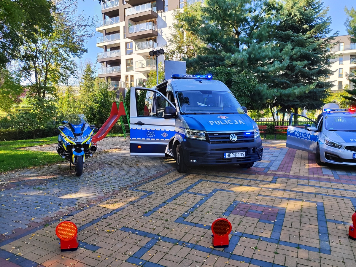 zdjęcie kolorowe: policyjne radiowozy i motocykl ustawione na placu przed przedszkolem