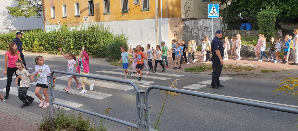 zdjęcie kolorowe: dzielnicowi z uczniami klas pierwszych podczas nauki przechodzenia przez przejście dla pieszych