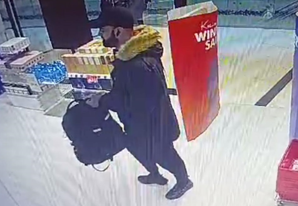zdjęcie kolorowe: mężczyzna ubrany w zimową kurtkę, czapkę z daszkiem i zarostem na twarzy wchodzi do sklepu