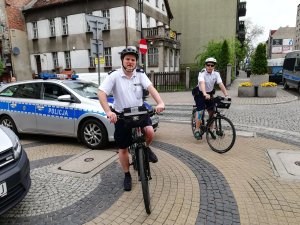 policjanci jadą na rowerach za nimi stoi radiowóz policyjny