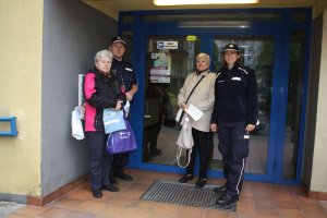 Na zdjęciu widać dzielnicowego z policjantką z zespołu profilaktyki jak stoją wraz z seniorami przed wejściem do budynku