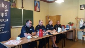 na zdjęciu widać czterech policjantów siedzących przy stole obok stoi baner KMP Katowice