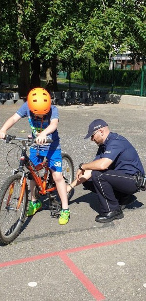na zdjęciu widać dziecko jadące na rowerze obok policjant kuca i ogląda oponę