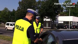 Zdjęcie kolorowe: dwóch umundurowanych policjantów katowickiej drogówki podczas kontroli czarnego pojazdu