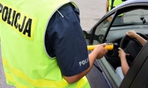 Zdjęcie kolorowe: policjant ruchu drogowego z urządzeniem do badania zawartości alkoholu w wydychanym powietrzu u kierującego pojazdem
