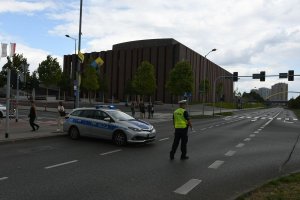 na zdjęciu widać radiowóz policyjny oraz policjanta który kieruje ruchem w tle budynek NOSPR