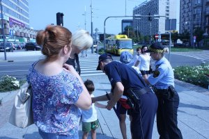 Na zdjęciu widać policjanta i strażnika miejskiego obok stoją kobiety z dzieckiem w tle widać autobus na ulicy