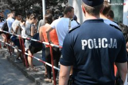 Zdjęcie kolorowe: policjant w umundurowaniu ćwiczebnym stojący, obok osób oczekujących na warsztaty szkoleniowe