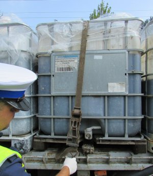 zdjęcie kolorowe: policjant wydziału ruchu drogowego sprawdzający zabezpieczenie pojemników typu mauser przez uszkodzone pasy transportowe