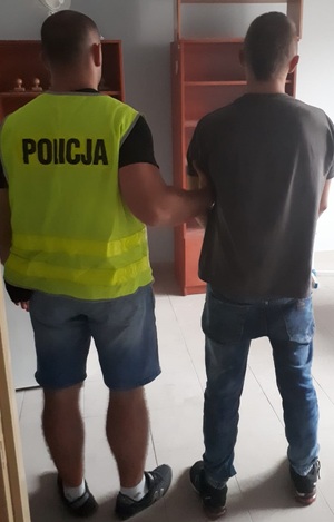 zdjęcie kolorowe: nieumundurowany policjant w odblaskowej kamizelce z napisem &amp;quot;Policja&amp;quot; z zatrzymanym mężczyzna