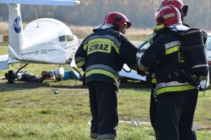 zdjęcie kolorowe: zdjęcie kolorowe: dwie osoby ranne leżące pod samolotem na płycie lotniska i trzech strażaków podczas akcji ratowniczej