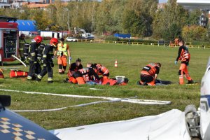 zdjęcie kolorowe: ratownicy medyczni i strażacy udzielający pomocy osobom rannym na tle wozu strażackiego