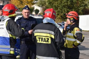 zdjęcie kolorowe: policjant i trzech strażaków ustalających kolejność działań podczas akcji ratowniczej