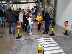 na kolorowym zdjęciu widać symulację przejścia dla pieszych obok stoi policjantka oraz kobieta z dzieckiem.