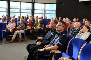 Na kolorowym zdjęciu widać Zastępce Komendanta Wojewódzkiego i Miejskiego Policji w Katowicach w tel siedzą ludzie na krzesłach w auli