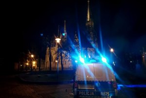 Na zdjęciu widać radiowóz z włączonymi sygnałami świetlnymi w tle stoi kościół