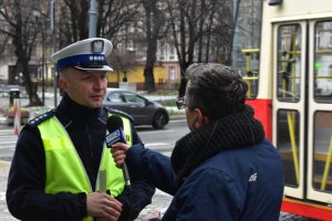 Na kolorowym zdjęciu widać policjanta ruchu drogowego który wypowiada się dla dziennikarza telewizji polskiej