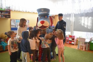 Na zdjęciu widać policjanta z maskotką sznupkiem i dzieci przytulające się do sznupka