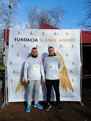 Na zdjęciu widać dwóch policjantów w stroju sportowym na tle log fundacji śląskie anioły