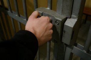 zdjęcie kolorowe: dłoń trzymająca klucz do zamka w drzwiach policyjnego aresztu