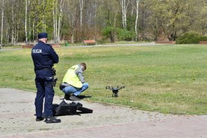 Na zdjęciu widać dwóch policjantów w parku oraz drona