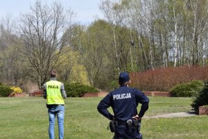 Na zdjęciu widać dwóch policjantów w parku oraz wypuszczonego drona,