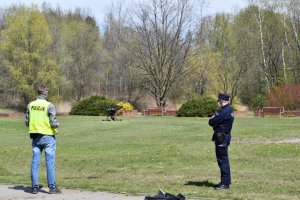 Na zdjęciu widać dwóch policjantów w parku oraz wypuszczonego drona,
