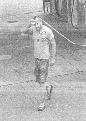 Na zdjęciu widać osobę podejrzaną o uszkodzenie ciała jak idzie przez stację paliw, jest ubrana w krótkie spodnie oraz koszulkę z krótkim rękawem