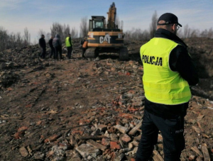 zdjęcie kolorowe: policjant na miejscu ujawnienia nielegalnego wysypiska śmieci